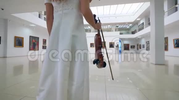 带着小提琴的女人正沿着艺术画廊走着视频的预览图