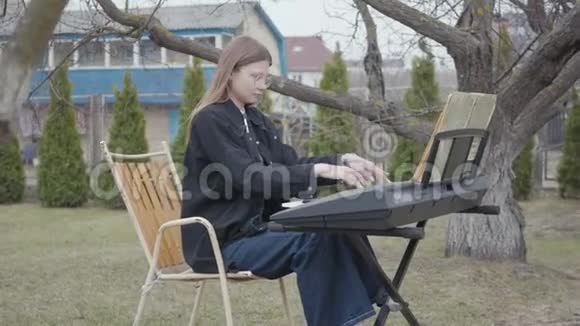 专业可爱的女钢琴家在后院的合成器上演奏古典钢琴音乐真人系列视频的预览图