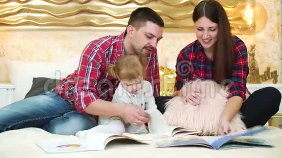 年幼的父母带着小女儿在家里在床上看书视频的预览图