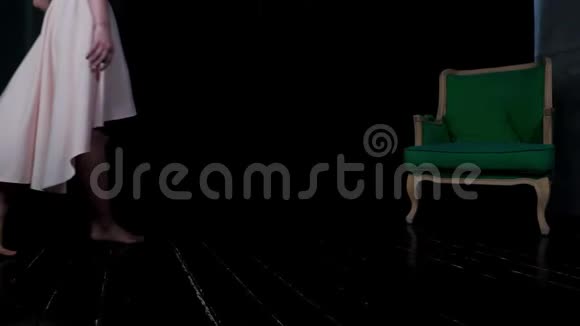 一个穿着三文鱼色连衣裙的女孩走在一个带绿色椅子的黑暗房间里视频的预览图