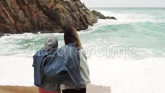 一对女孩夫妇穿着一件夹克看着美丽的暴风雨海景视频的预览图