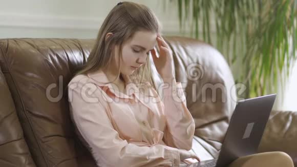 专注优雅的女孩坐在皮革沙发上在笔记本电脑键盘上打字现代青少年的休闲视频的预览图