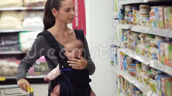 一位年轻的母亲带着她的孩子在一家超市商店买婴儿食品育儿的概念视频的预览图