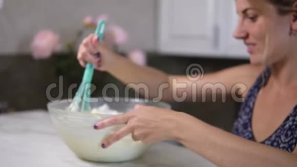 年轻女子用厨房里的搅拌器在碗里搅拌面团然后看着镜头视频的预览图
