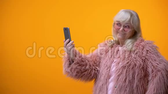 穿着有趣的粉红色外套的开朗的高级女士在智能手机上自拍玩得很开心视频的预览图