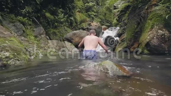 年轻人在热带雨林中的热带瀑布流的河水上游泳快乐的男人享受水流视频的预览图