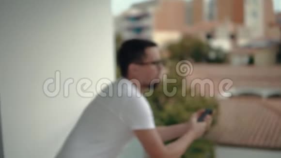 一个英俊的男人独自站在阳台上用智能手机视频的预览图