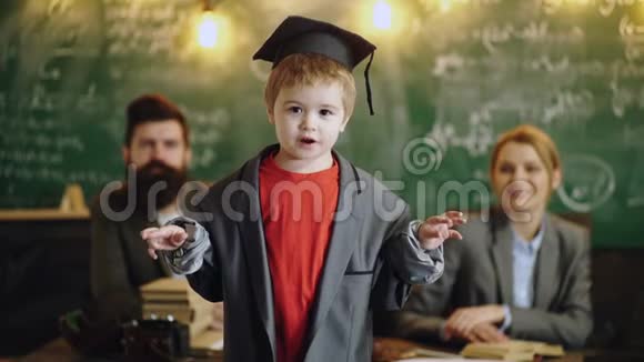 戴着学术帽和西装的男孩在父母和学校董事会的背景下说话和拍手小男孩视频的预览图