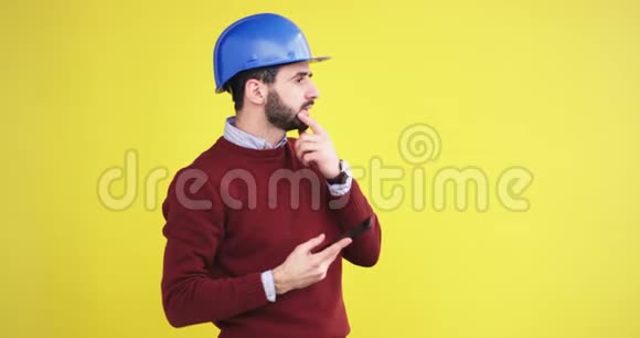 年轻的工程师带着蓝色的头盔在工作室里用黄色的背景墙拍照视频的预览图