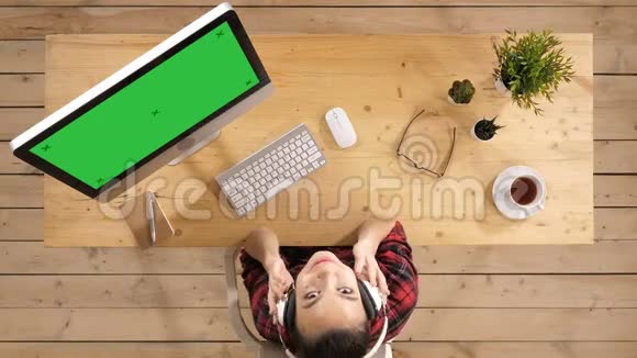 年轻漂亮的女人在她的工作场所听音乐仰望镜头绿色屏幕模拟显示视频的预览图