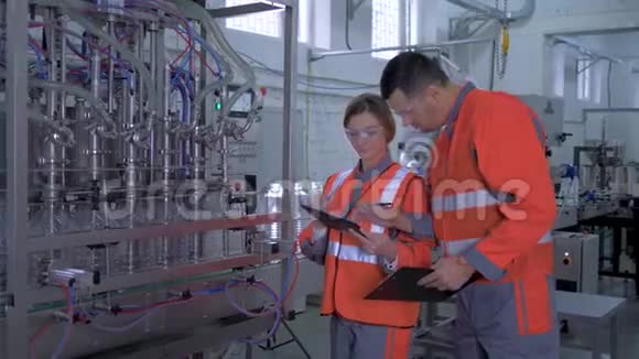 工厂行业年轻的女性和男性工业工人把手里拿着数字平板电脑的工作服靠近自动视频的预览图