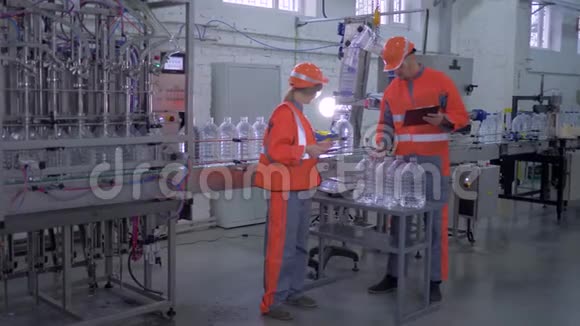工厂工人男男女女进入头盔和整体附近的输送线装瓶矿泉水塑料瓶视频的预览图