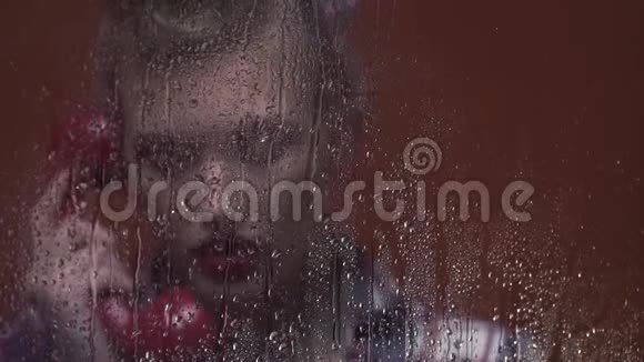 复古风格的金发女人在潮湿的窗户后面用一个旧的红色电话交谈视频的预览图