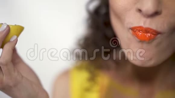 特写肖像丰满的嘴唇与明亮的橙色口红咬酸片柠檬的乐趣慢动作视频的预览图