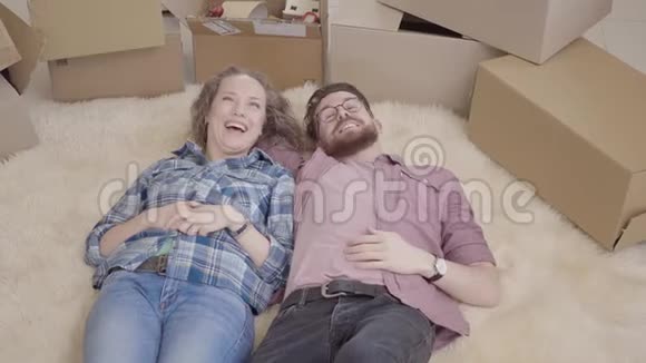 开朗的年轻人讨论躺在蓬松地毯上的公寓内部布局已婚夫妇搬进视频的预览图