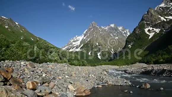 一条被林地和高岩石山脉环绕的暴风雨山河的岩石海岸视频的预览图
