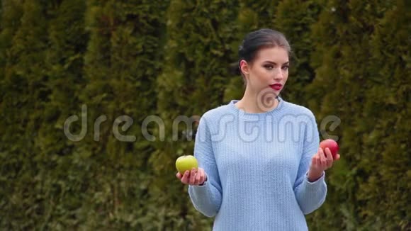 在绿苹果和红苹果之间选择穿蓝色夹克的漂亮年轻女子肖像决定咬绿苹果视频的预览图