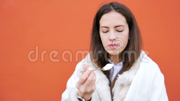 漂亮迷人的女孩在红墙背景上用勺子吃酸奶视频的预览图