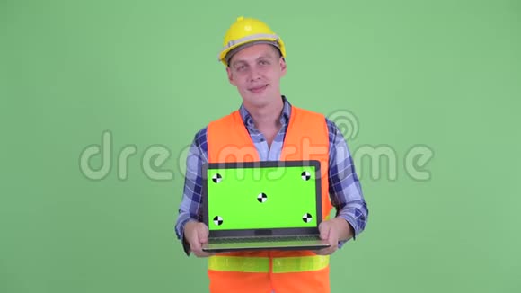快乐的年轻建筑工人一边思考一边展示笔记本电脑视频的预览图