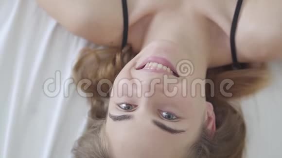 可爱的年轻快乐的白种人女人有着不同颜色的眼睛躺在床上早上用毯子盖住她的脸视频的预览图