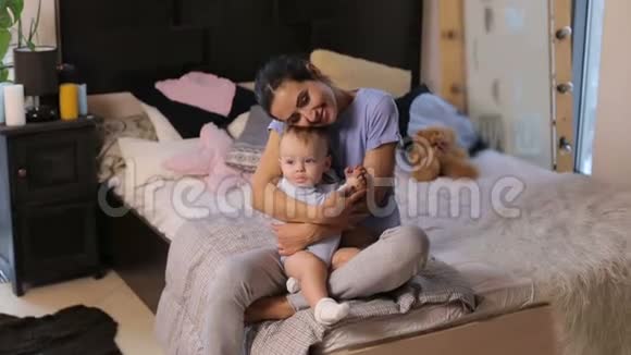 一位可爱的年轻母亲在舒适的卧室里拥抱她的小儿子的肖像视频的预览图