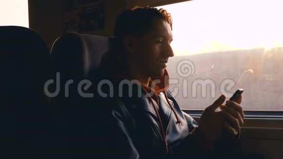 年轻男子在火车上使用智能手机坐在窗户对面美丽的日落视频的预览图