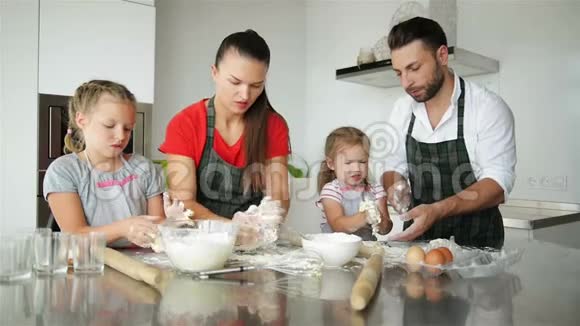 可爱的小女孩和他们美丽的父母在家厨房做饭时揉捏面团和微笑视频的预览图