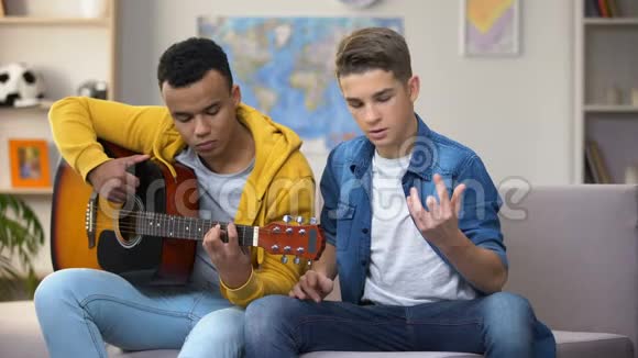 非裔美国青少年教白种人朋友弹吉他爱好视频的预览图