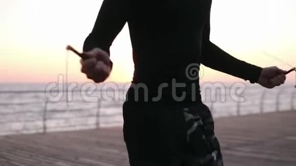 近距离拍摄白种人运动员穿着黑色运动服跳过跳绳的躯干太阳照耀着视频的预览图