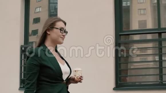 年轻女子拿着咖啡杯走在城市街道上窗楼背景视频的预览图