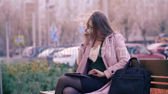 现代城市的商务女性在手机上聊天在长椅上使用平板电脑视频的预览图