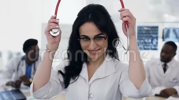 年轻女医生把听诊器放在颈部的肖像医院背景上的工作人员团队视频的预览图