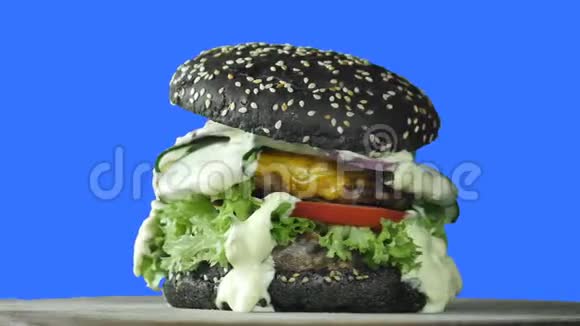 一个大的多汁的汉堡里面有一个黑面包上面撒着芝麻在一个孤立的蓝色背景下旋转一个汉堡里塞满了视频的预览图