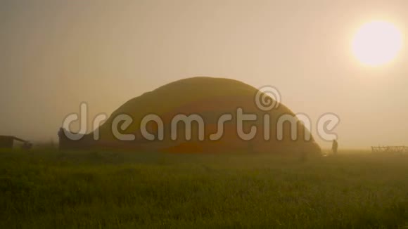 充气热气球准备日出飞行早上雾蒙蒙的草地上晶莹的露水视频的预览图