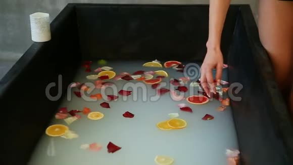 女性双手特写将柑橘片和玫瑰花瓣混合在奶水中视频的预览图