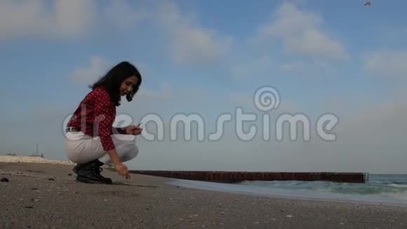 女孩坐在海滩上把鹅卵石抛在海上对着天空视频的预览图
