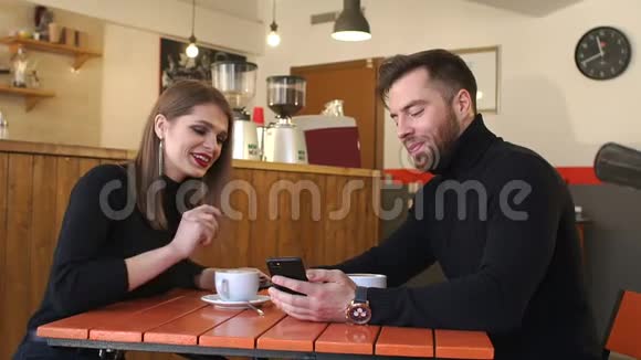 一对年轻快乐的夫妇在咖啡店里休息看着手机屏幕视频的预览图