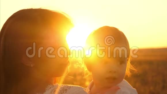 妈妈把她的小女儿抱在怀里欢乐的一家人在公园温暖的夏日傍晚看日落视频的预览图