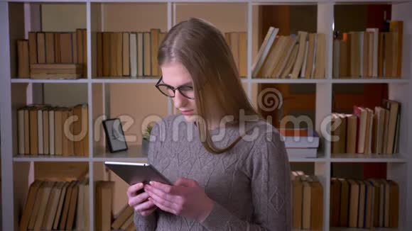 年轻漂亮的女学生戴着眼镜用平板电脑微笑着看着镜头特写照片视频的预览图