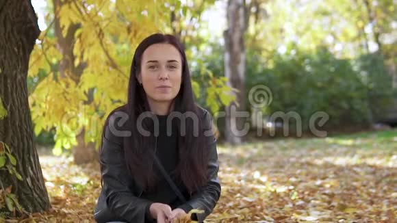一个可爱的女孩的肖像她在秋天的公园里抛出黄色的叶子笑得很漂亮视频的预览图