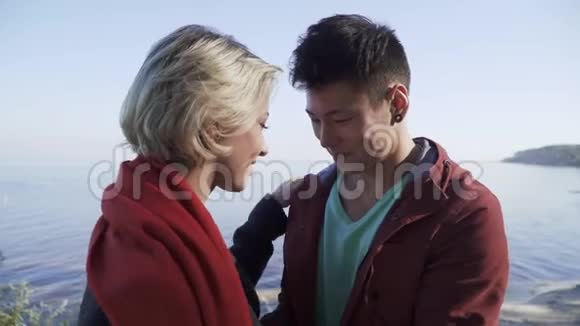 在悬崖松树和湖泊的背景下年轻的多民族微笑的情侣在爱情中接吻不同种族的接吻视频的预览图