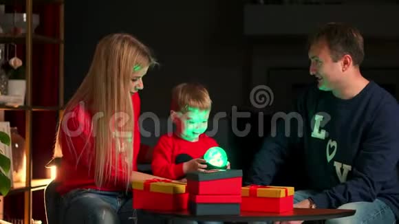 圣诞快乐假期快乐可爱的孩子和父母打开礼物穿睡衣的男孩在附近玩视频的预览图
