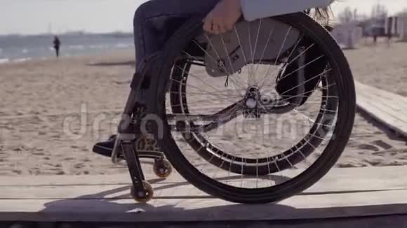 轮椅上的年轻残疾妇女在春季或春季在靠近海边的木制坡道旁为残疾人移动视频的预览图