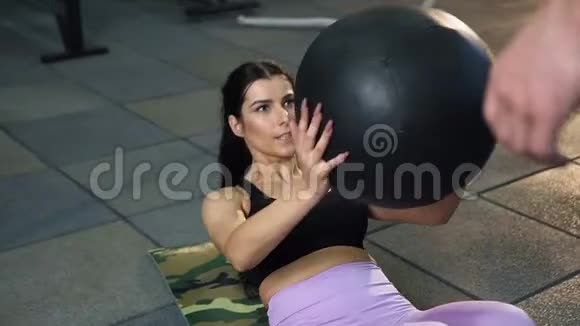 美丽的运动女性与男性教练一起用健身操球做腹肌运动视频的预览图