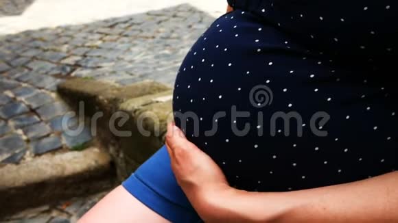 孕妇坐着穿着圆点孕妇装用手抚摸着肚子视频的预览图