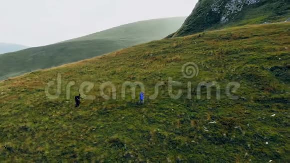 空中飞行高于人们沿着小径徒步旅行两位朋友夏季探险之旅在山地自然户外4k无人驾驶飞机视频的预览图
