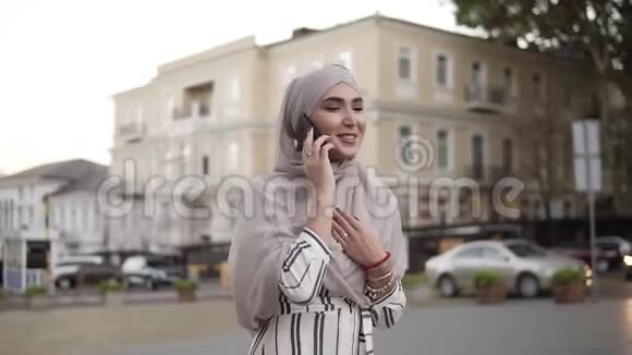 戴着头巾化妆的穆斯林妇女走在街上在一个美丽的古老经典的背景下打电话视频的预览图