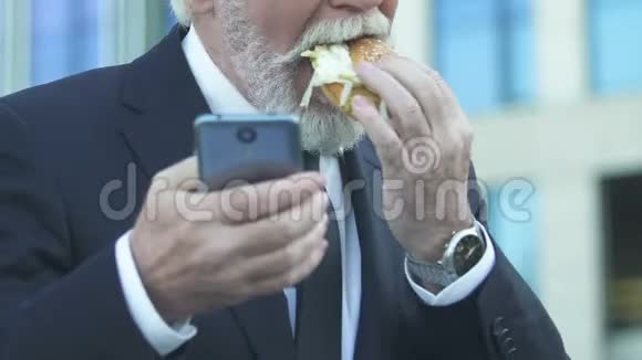 商人在使用电话时吃汉堡由于繁忙的生活方式营养不良视频的预览图