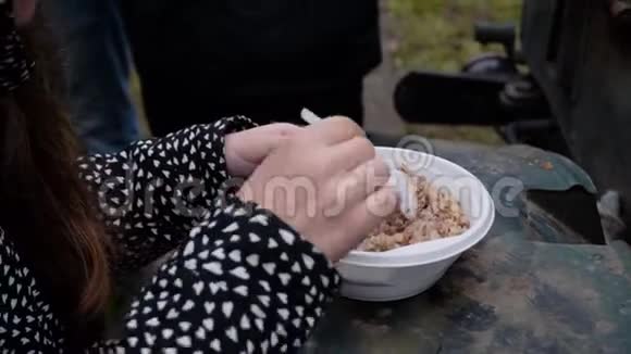 穿夹克的女孩正在吃一个士兵在野战厨房煮塑料碗里的麦片在新鲜空气中进食视频的预览图