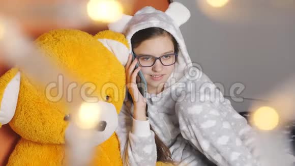 在圣诞节假期十几岁的女孩穿着温暖的睡衣和一个朋友在手机上聊天视频的预览图